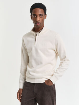 A man looking at the camera wearing a cream Gant half zip and a pair of dark trousers